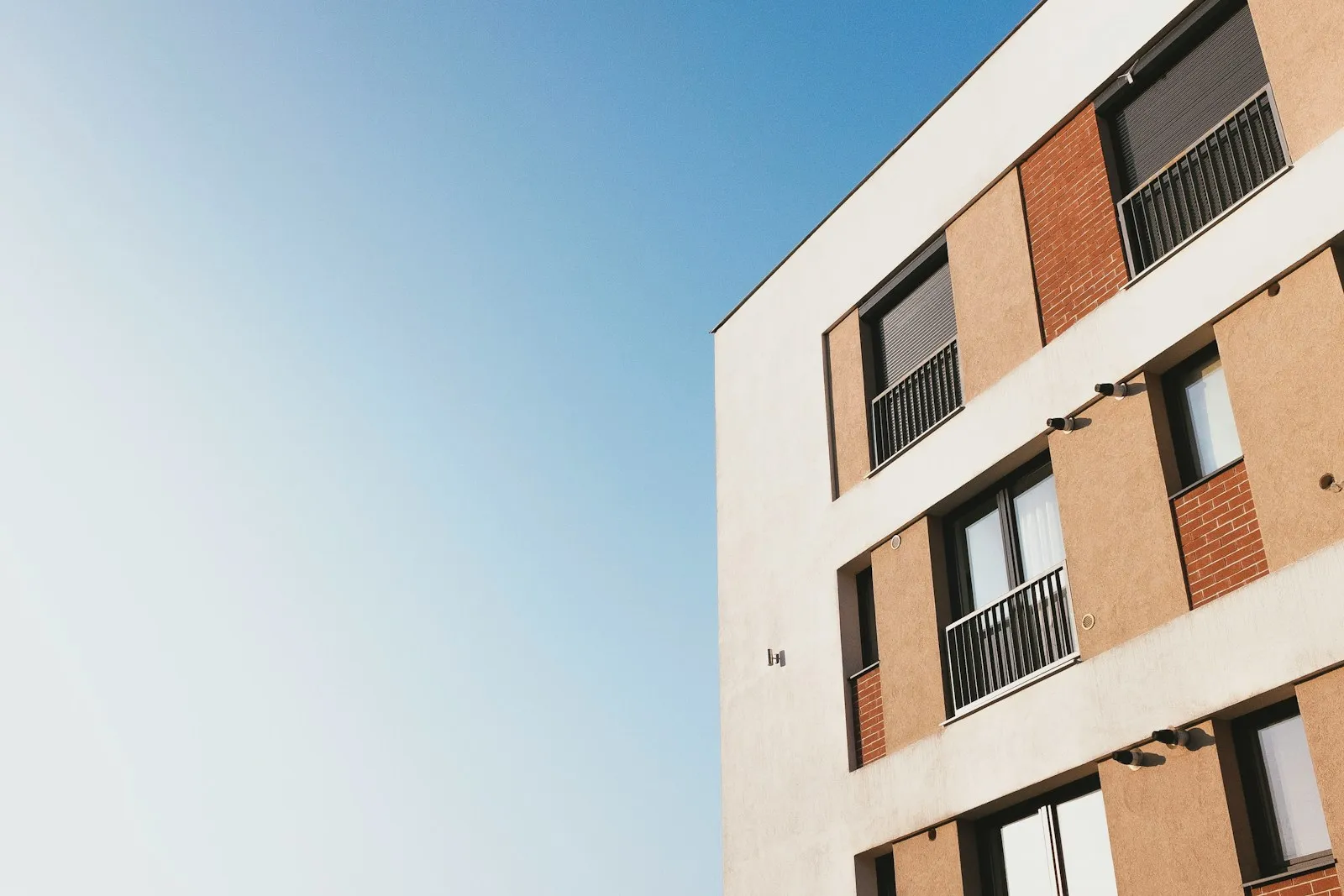 Un immeuble d'habitation récent, blanc et brique, avec balcons et volets, sous un ciel bleu