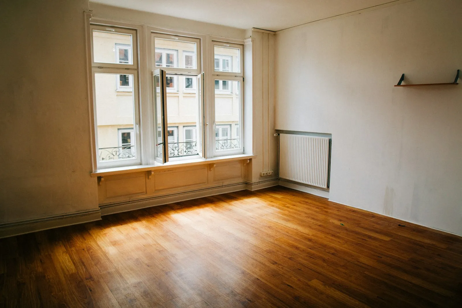 Une pièce vide et lumineuse avec parquet et grandes fenêtres, prête à être visitée
