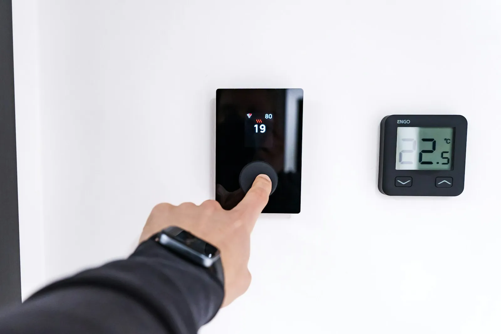Une main règle un thermostat numérique mural dans un intérieur lumineux