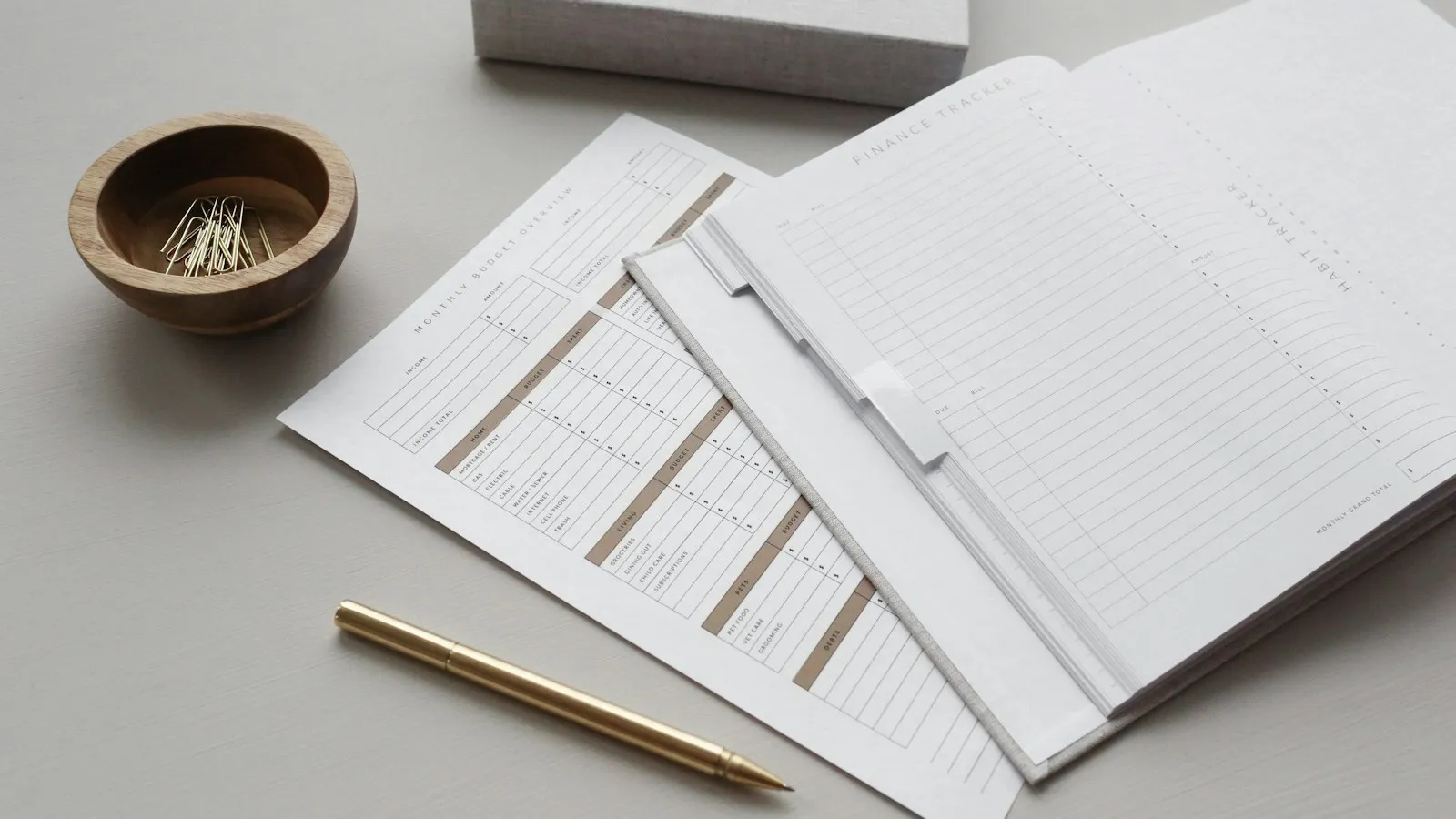 Des feuilles de budget et un carnet de suivi posés sur un bureau clair, avec un stylo doré