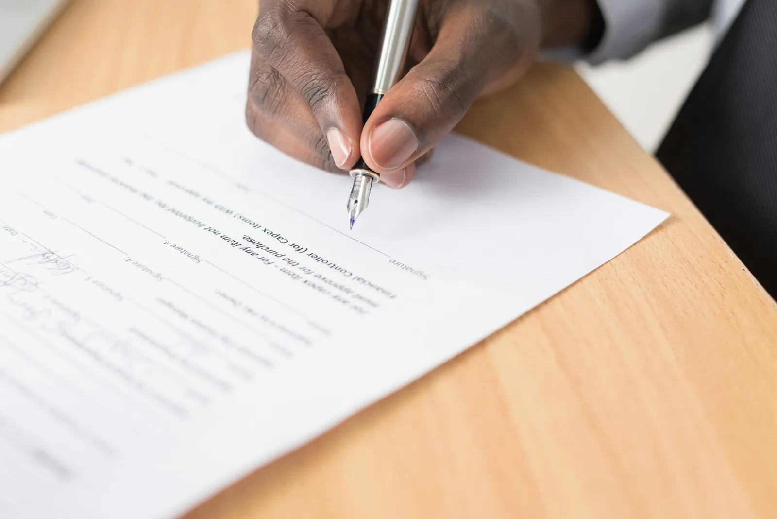 Une main signe un acte avec un stylo plume sur un bureau en bois clair