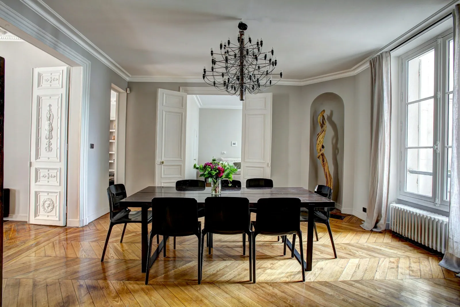 Un salon parisien meublé avec parquet en point de Hongrie, moulures et grandes fenêtres