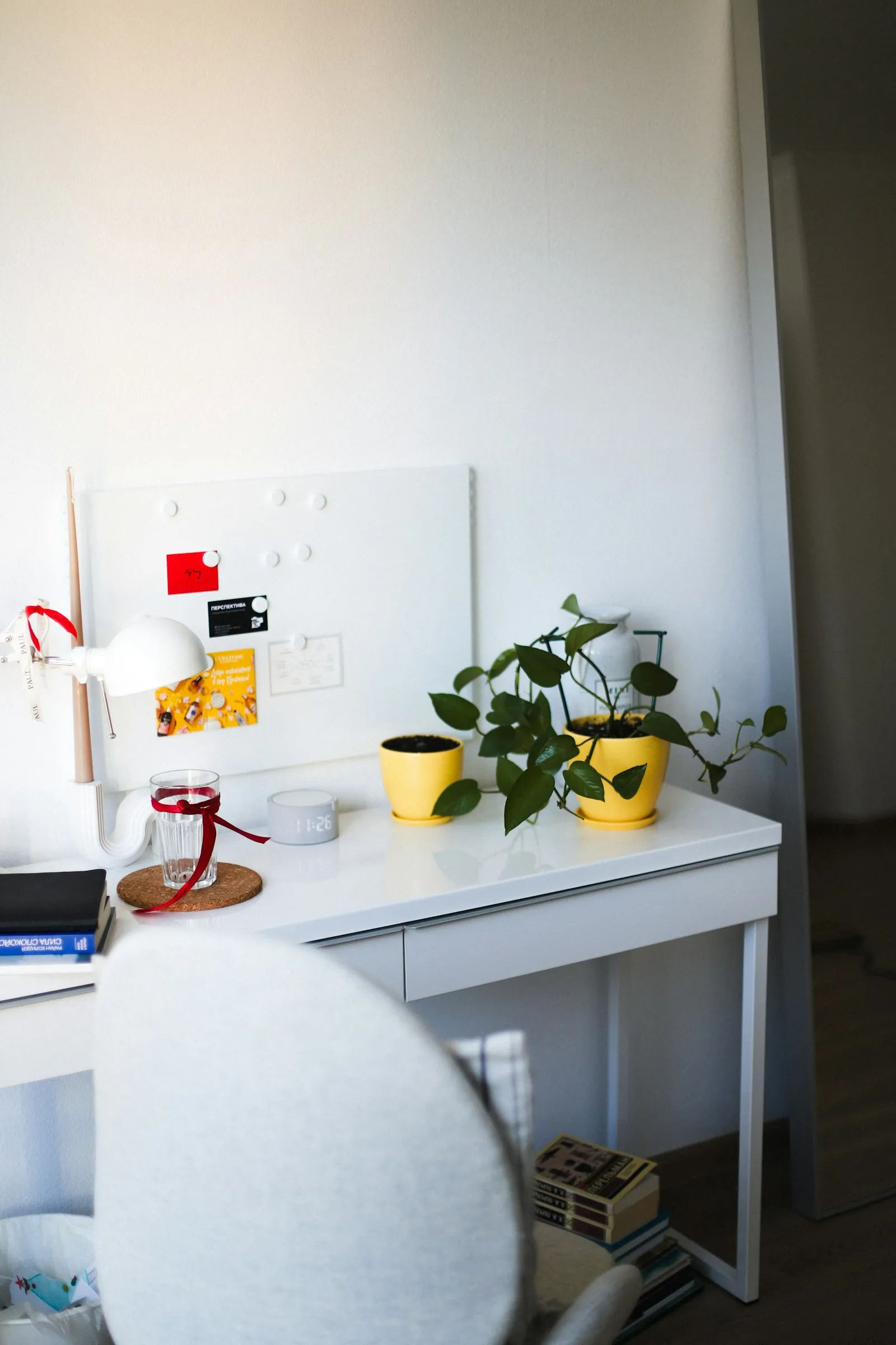 Un bureau blanc d'étudiant avec une lampe, des plantes et des livres, dans une pièce lumineuse