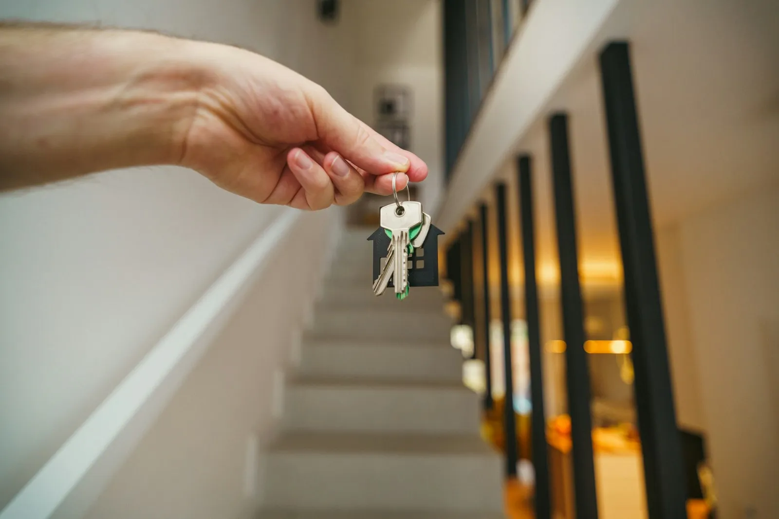 Une main tend les clés d'un logement avec un porte-clés en forme de maison, devant un escalier