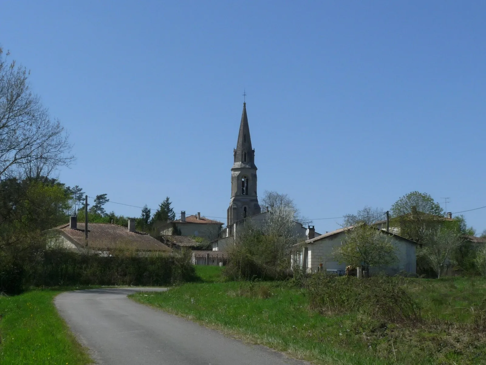 Le clocher de l’église Saint-Étienne au-dessus des maisons de Chamadelle, vu depuis une petite route