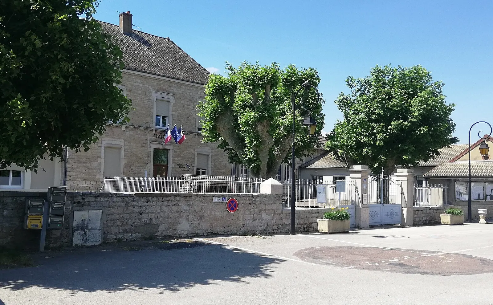 La mairie et l’école de Marnay derrière leur mur de pierre, sous un ciel bleu