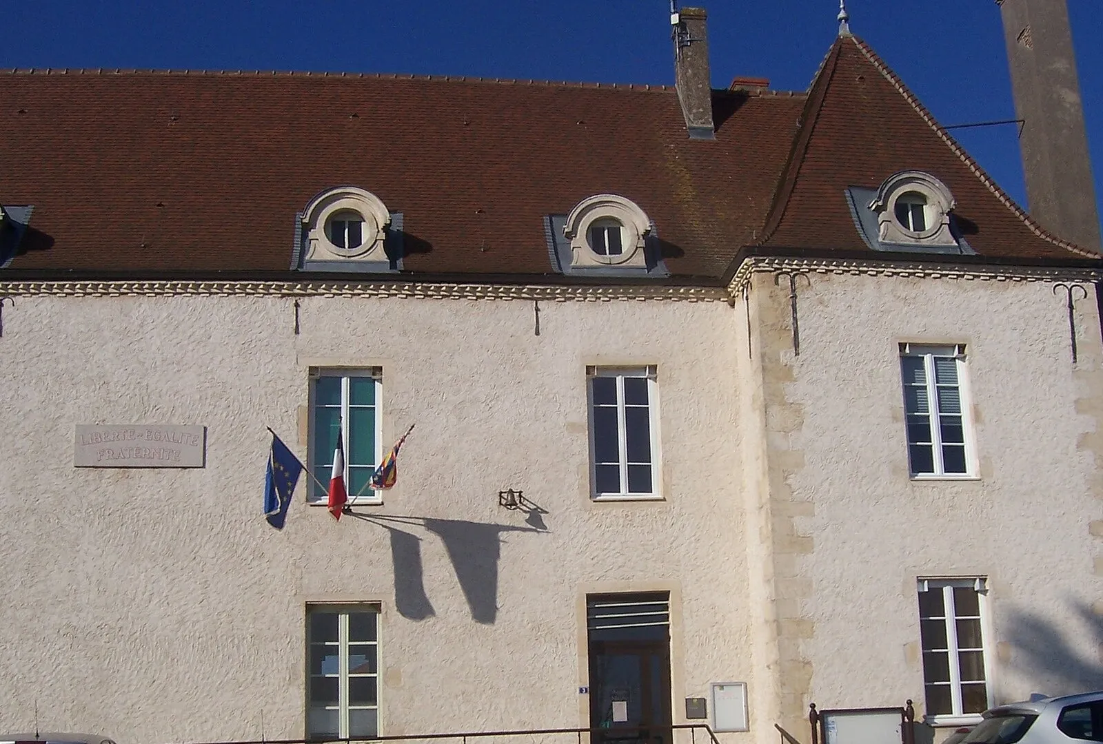 La mairie de Sassenay, longue façade aux lucarnes rondes, sous un ciel bleu